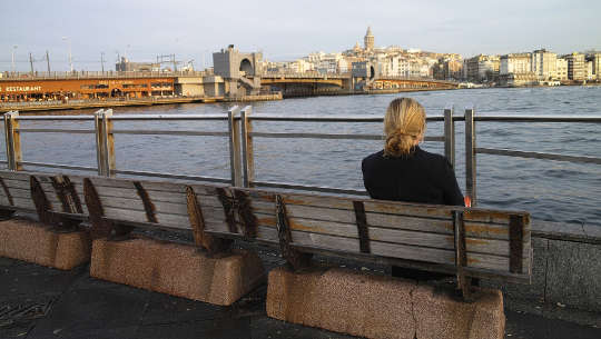 woman sitting alone on a bench facing the water and a city skyline