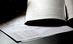 an astrology chart, an open book and a pen